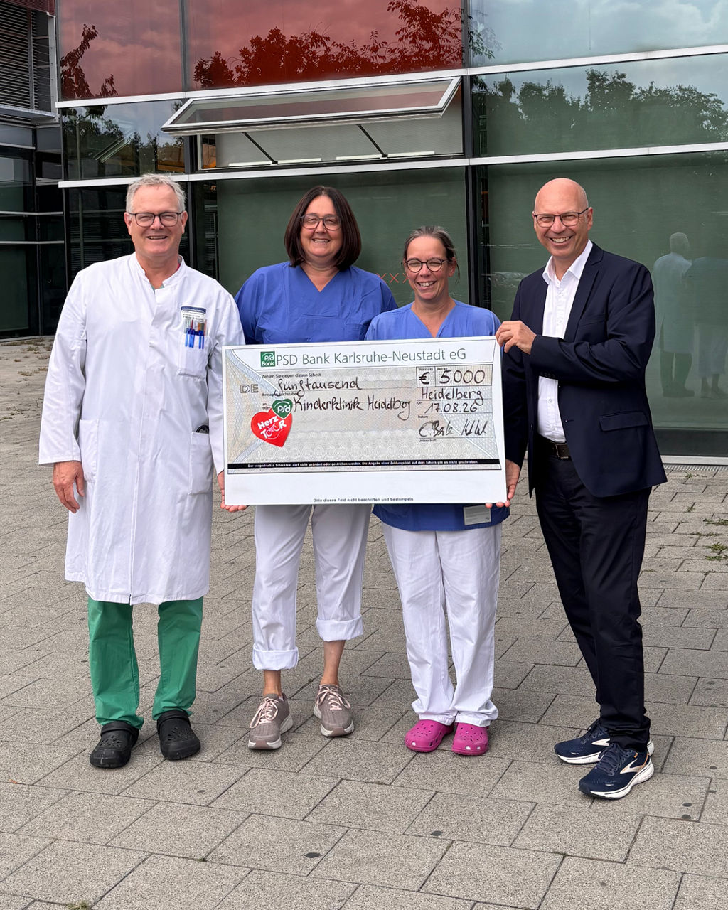 Drei Mitarbeiter der Heidelberger Klinik und unser Mitarbeiter Holger Morlock halten einen Spendenscheck vor sich.