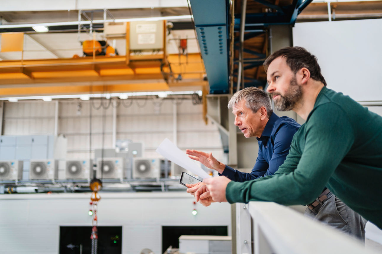zwei Männer stehen erhöht und schauen in eine Fertigungshalle