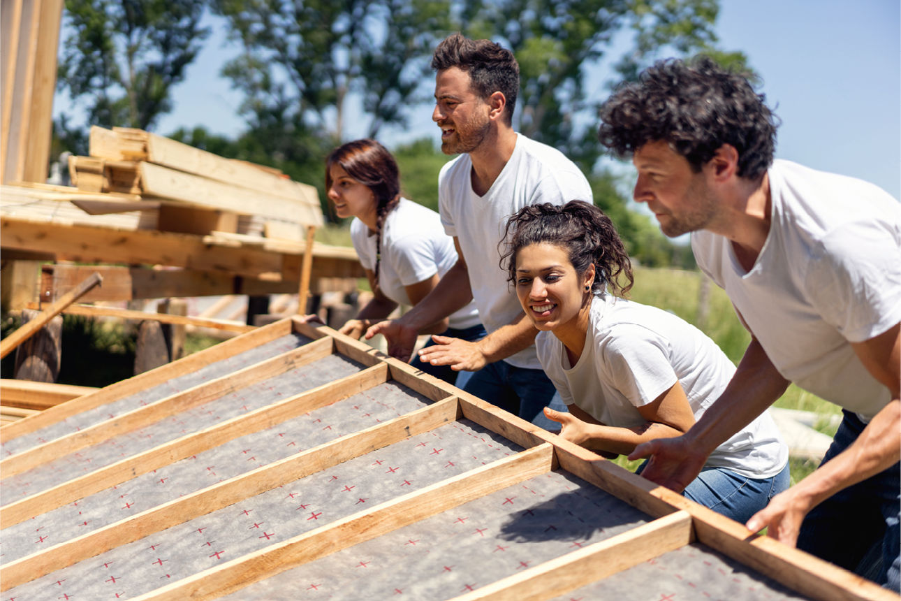 vier junge Leute heben gemeinsam ein vorgefertigtes Holzbauelemt an
