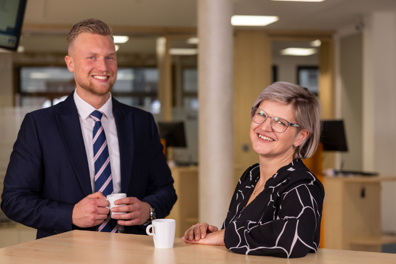 Junger Mann und Frau stehen mit Kaffeetasse am Infopoint