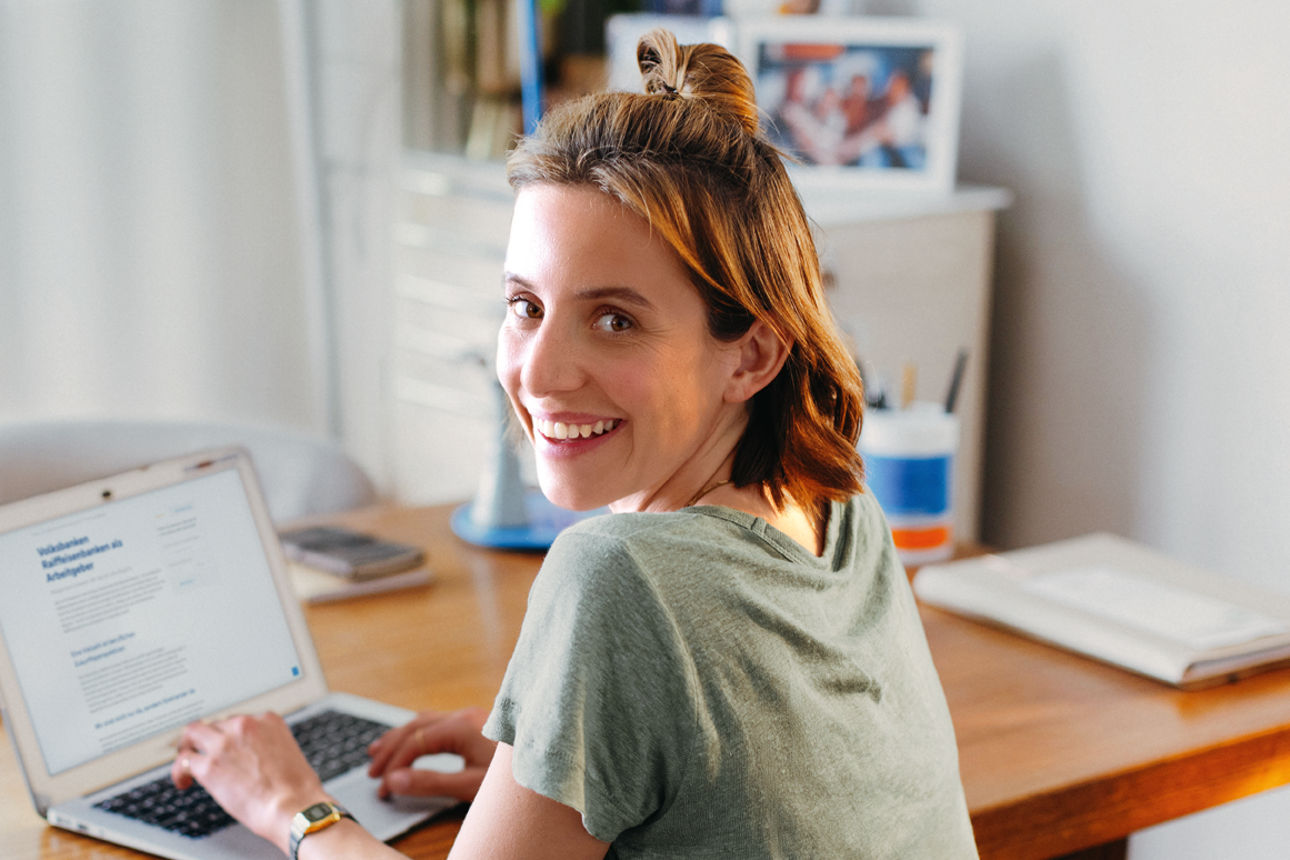 Eine Frau Laptop sitzt lächelnd an ihrem Arbeitsplatz