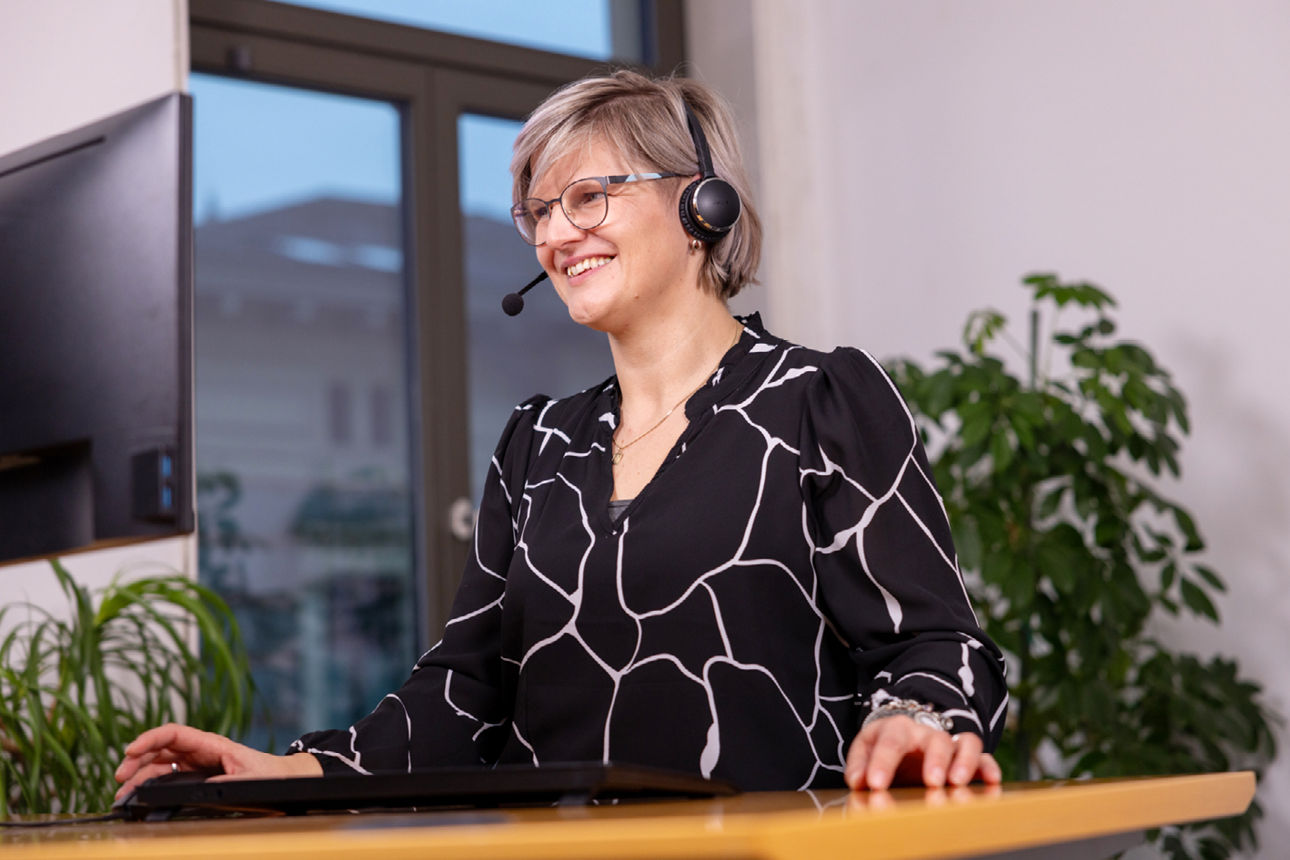 lächelnde Frau mit Headset steht am Schreibtisch 