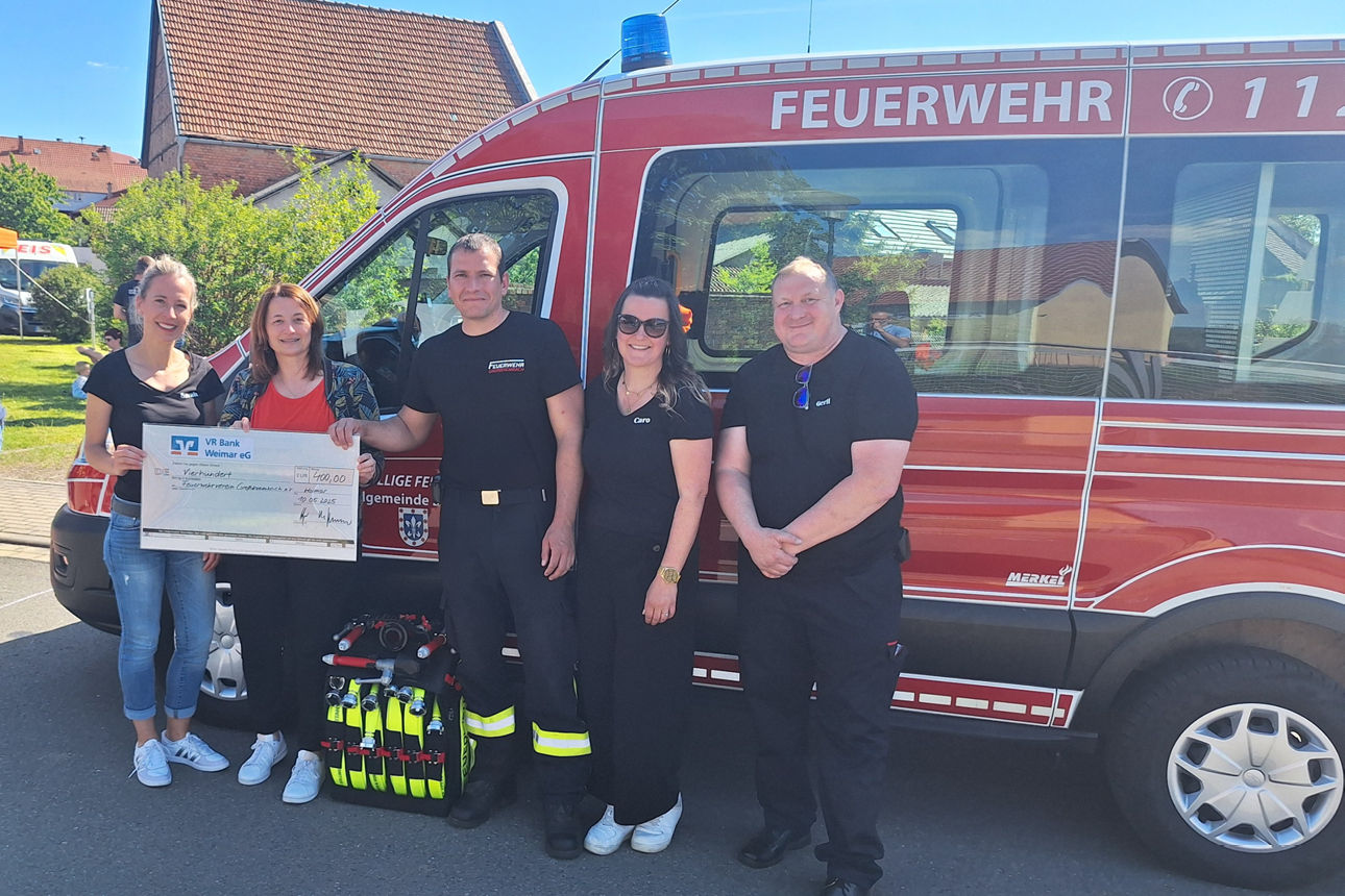 5 Personen stehen vor einem Feuerwehrauto und lächeln