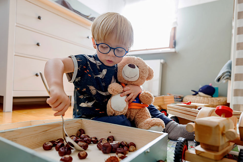 Kleiner Junge spielt in seinem Kinderzimmer und hat dabei den TeilhaBÄR als Kuscheltier in der Hand