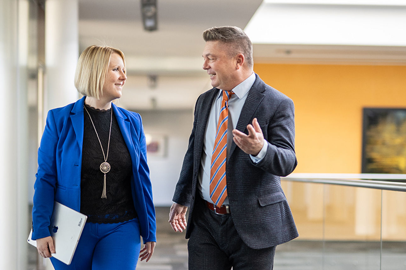 Zwei Kollegen gehen über einen Gang und tauschen sich aus