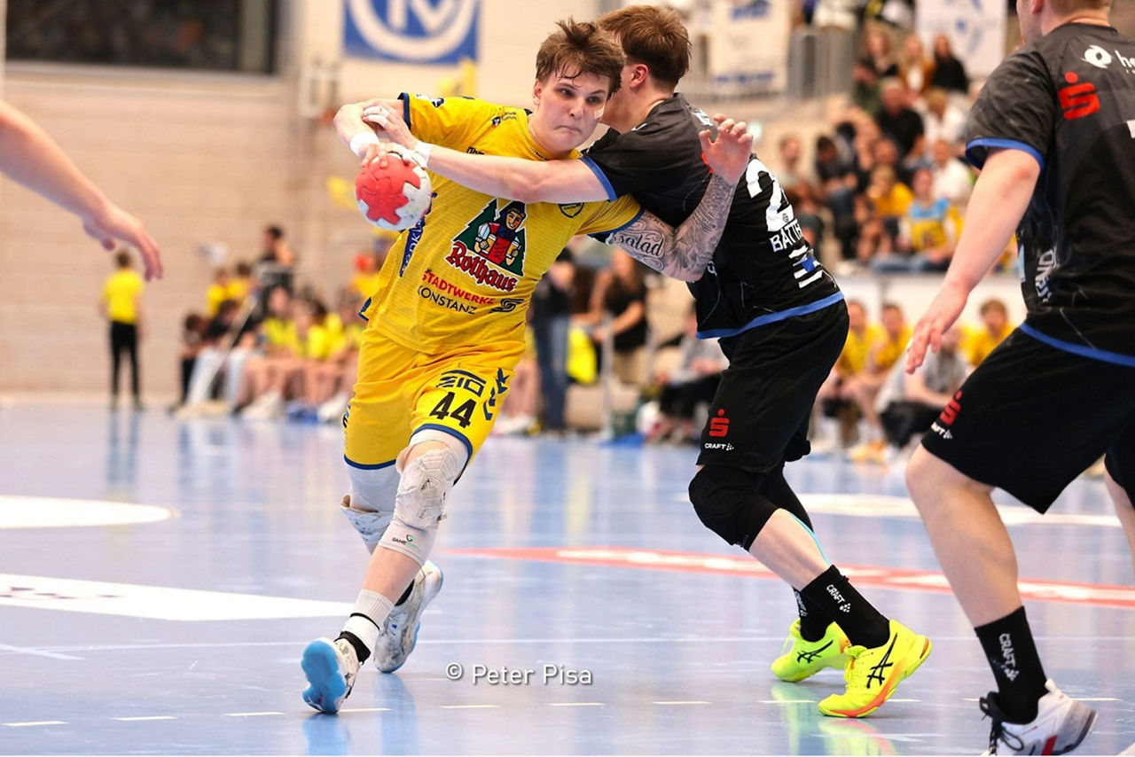 Ein angreifender Handballe mit dem Ball in der Hand wird von einem Verteidiger attackiert.