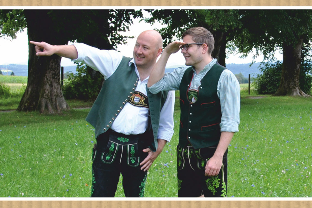 Zwei Männer stehen auf einer Wiese und schauen in die gedeutete Richtung