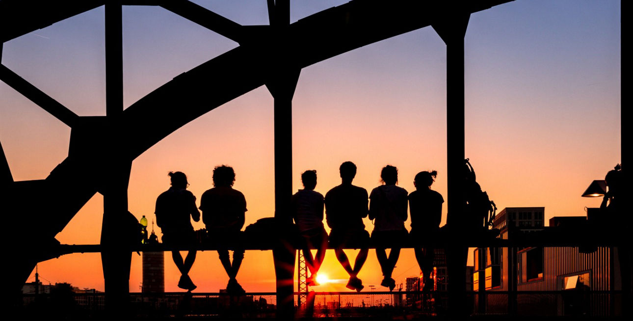 Menschen sitzen auf der Hackerbrücke und blicken in den Sonnenuntergang