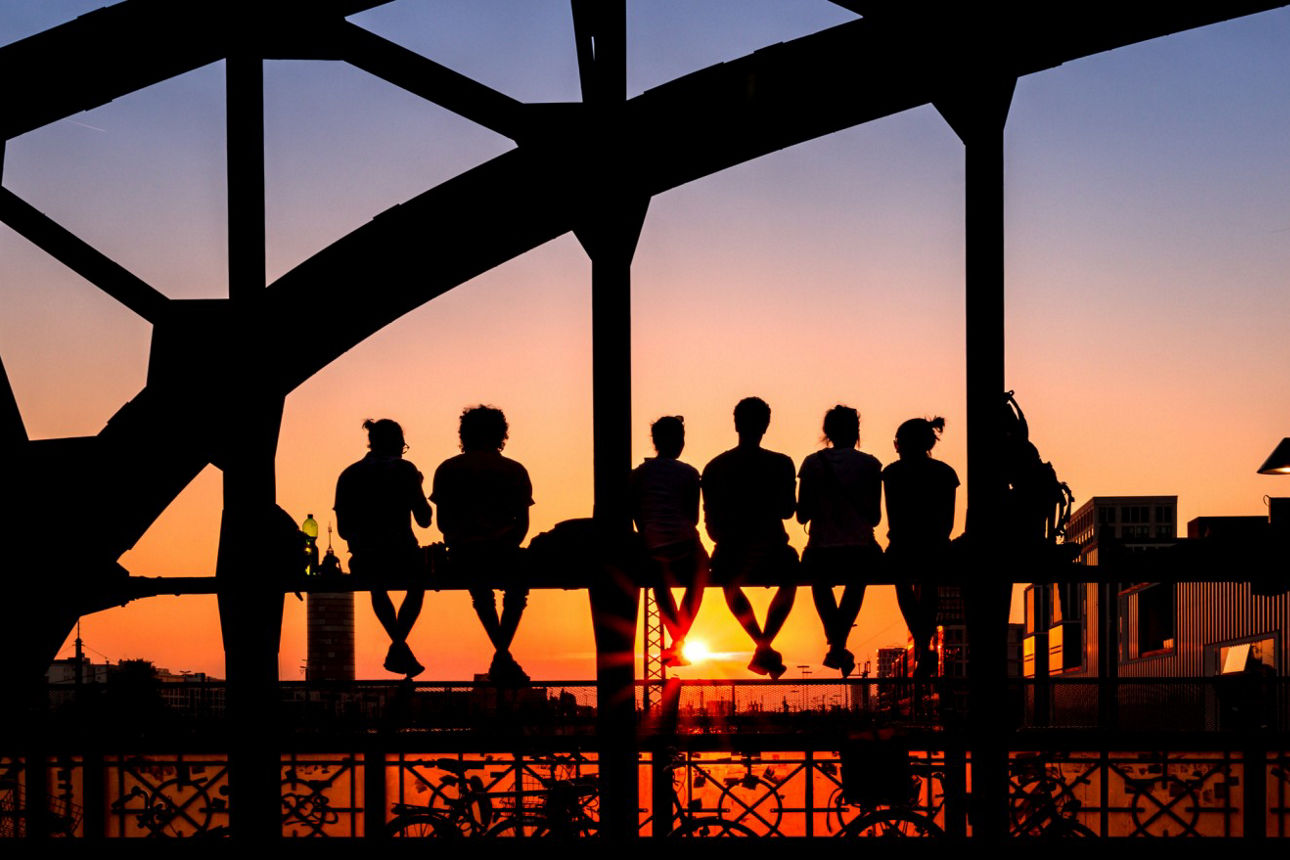 Menschen sitzen auf der Hackerbrücke und blicken in den Sonnenuntergang