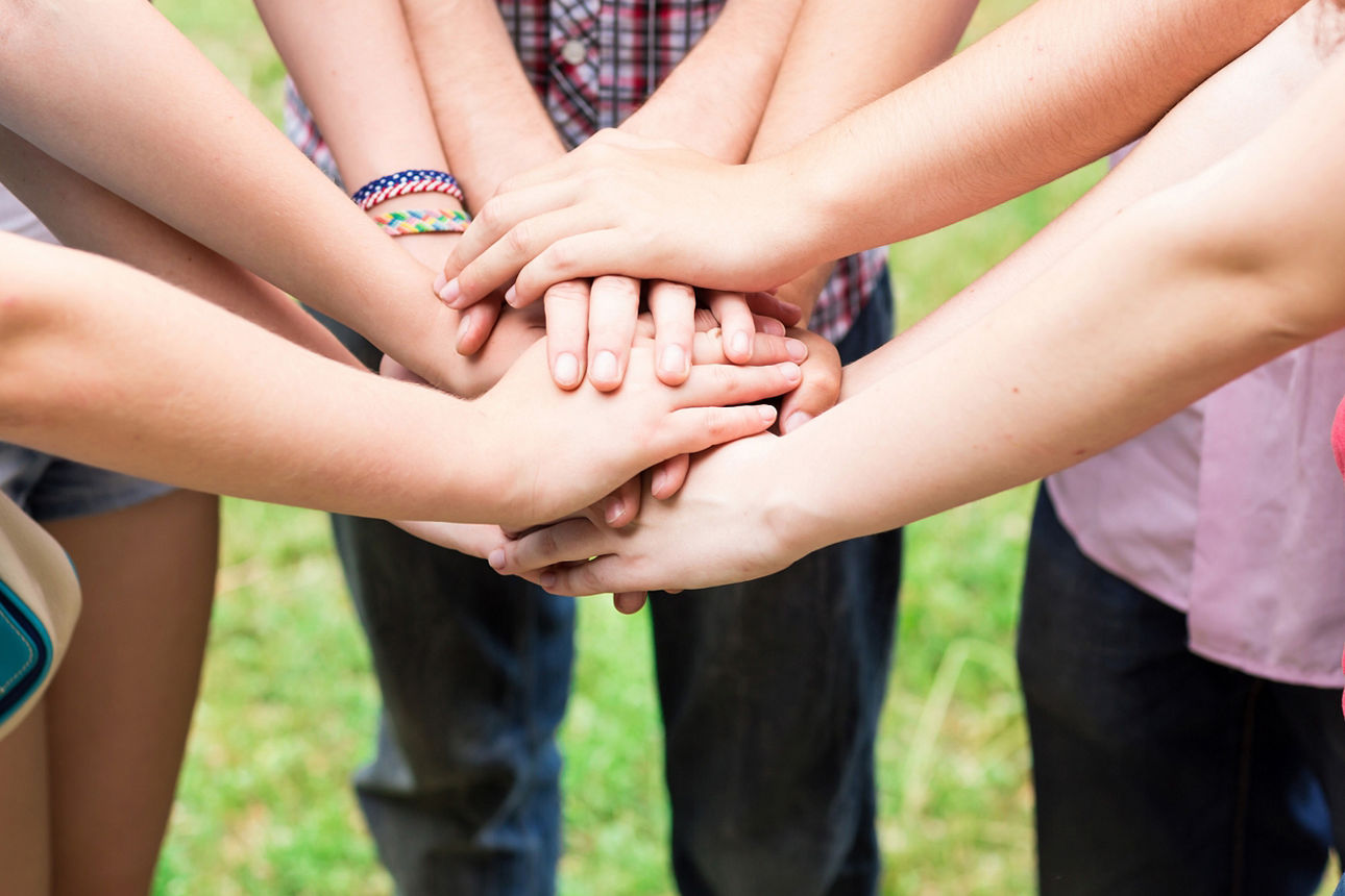 Gruppe von Menschen steht im Kreis und legt ihre Hände übereinander in die Mitte