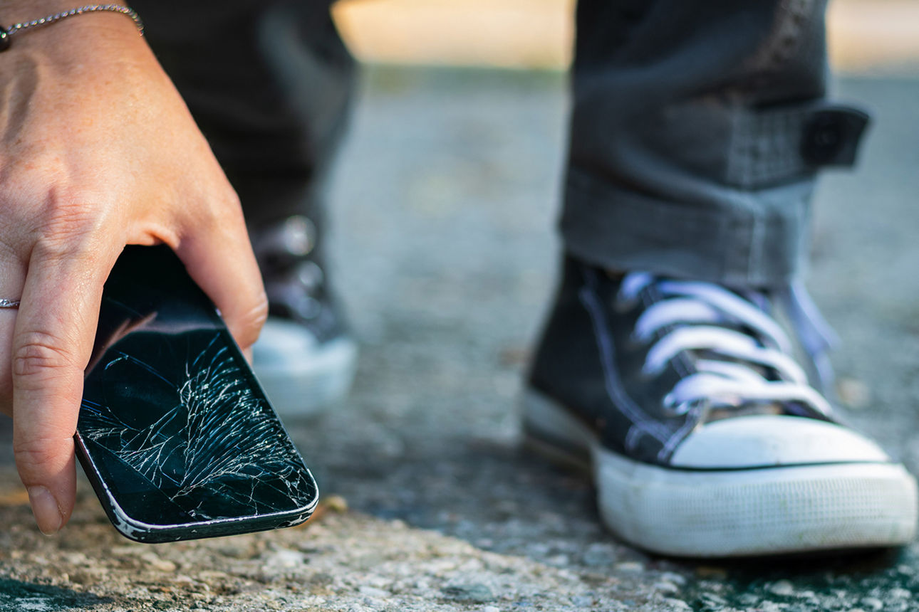 Person hebt zerbrochenes Smartphone auf