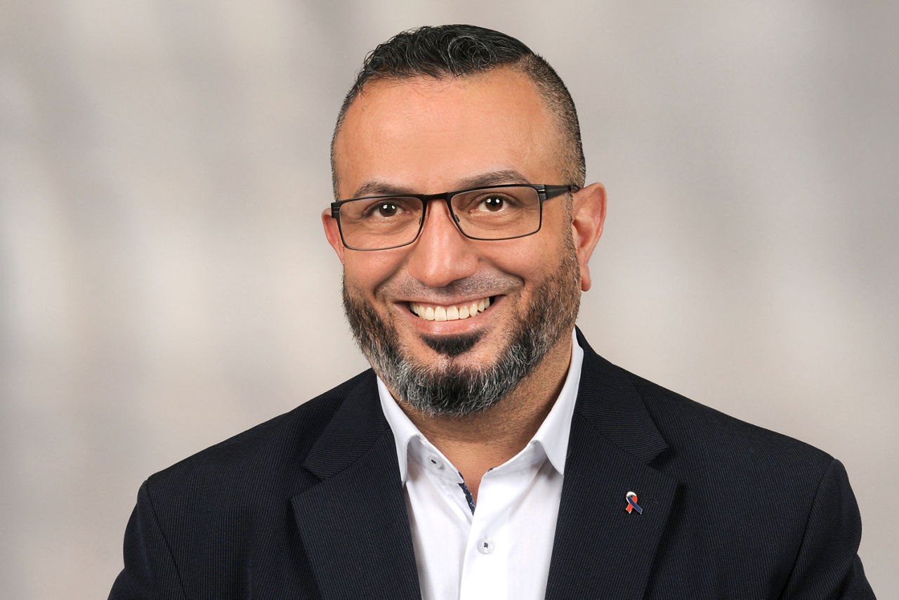 Mann mit Brille und Bart trägt schwarzen Anzug mit weißem Hemd und Anstecknadel mit französischer Flagge