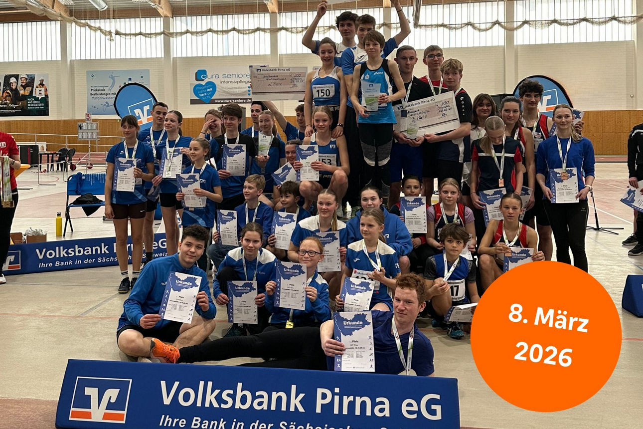 Große Gruppe Sportler in Turnhalle hält stolz Urkunden hoch hinter einer Bande mit Volksbank-Logo