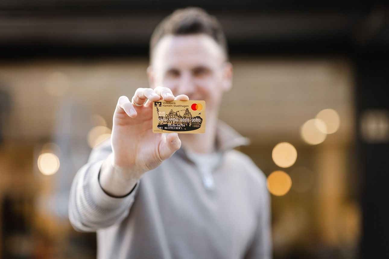 Eine Person hält eine goldene Kreditkarte mit Mastercard-Logo in die Kamera.