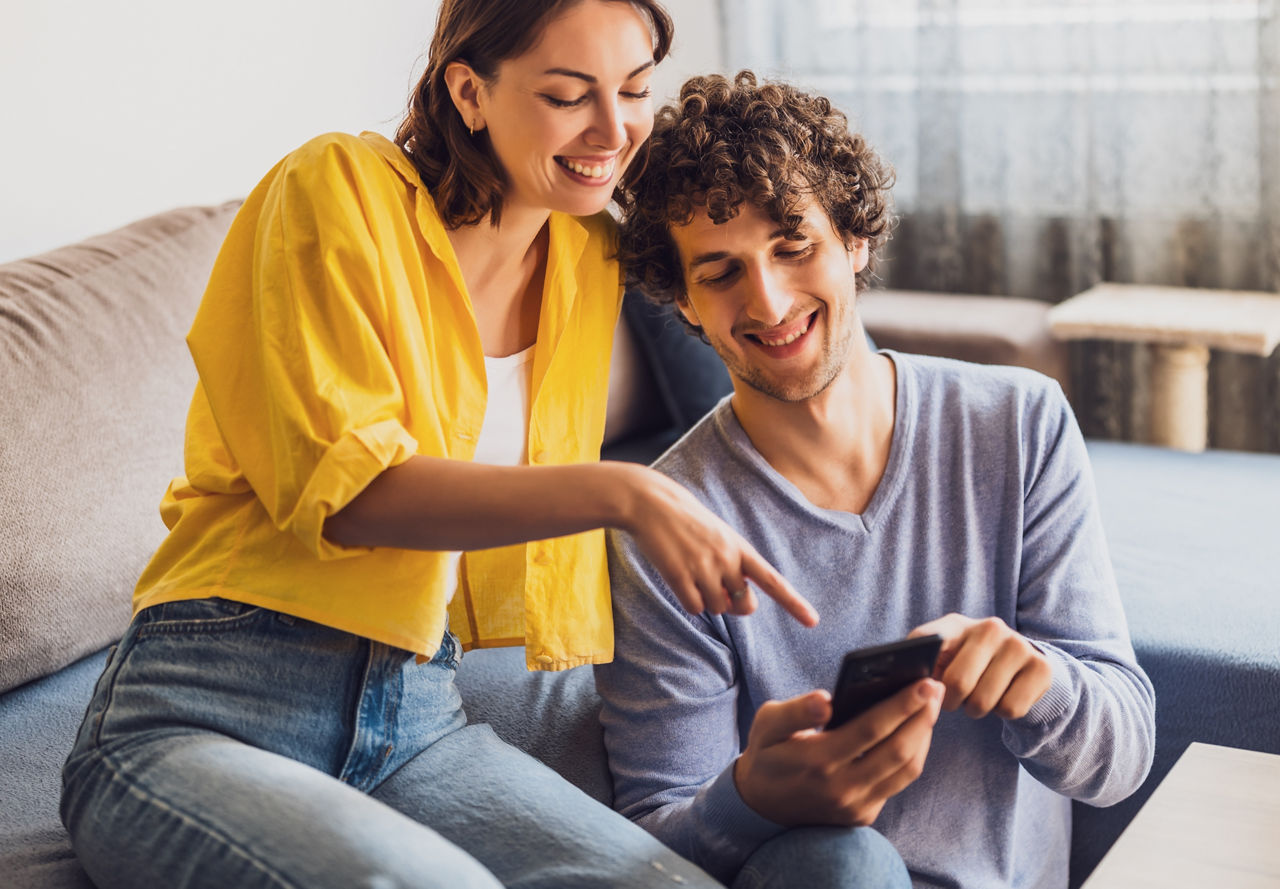 Pärchen Zuhause auf der Couch und schauen aufs Handy