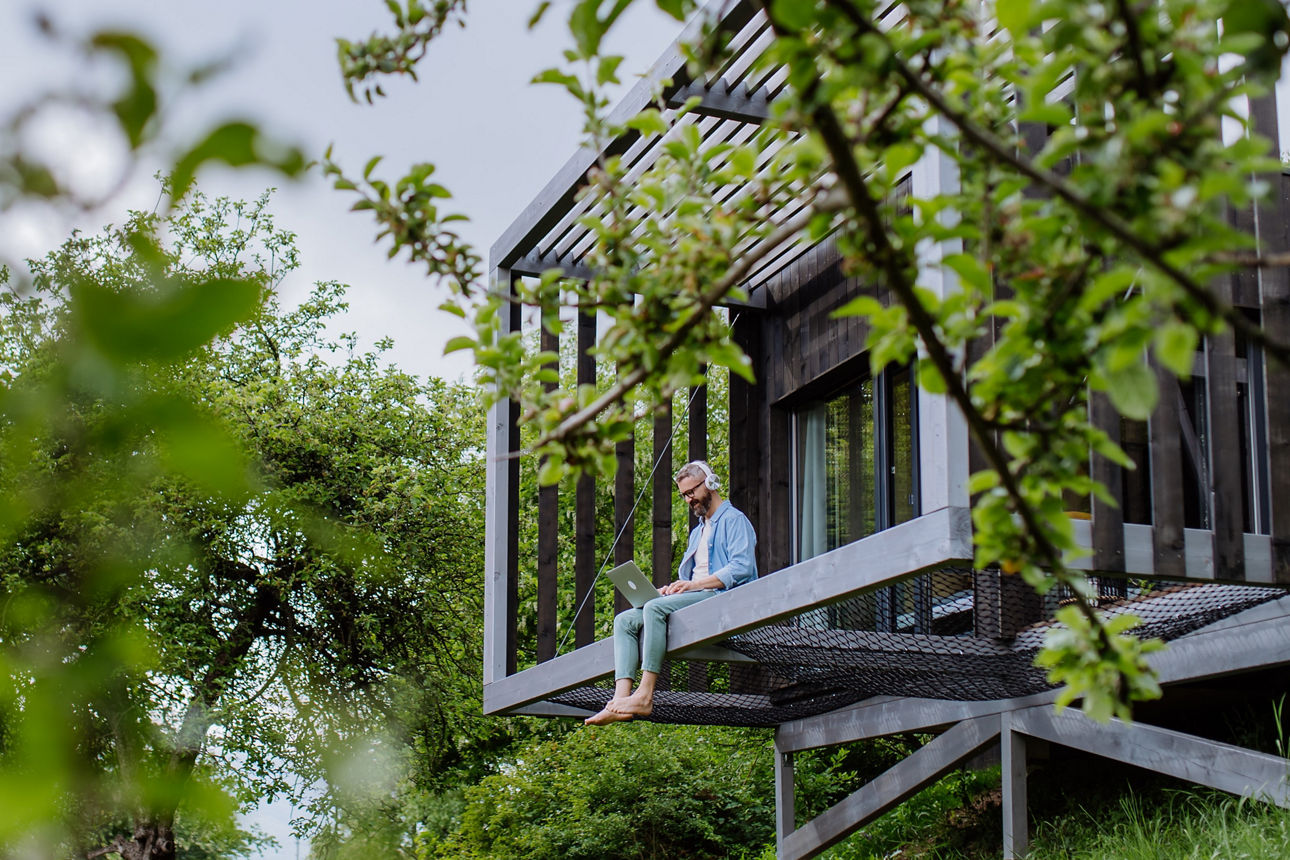 Mann mit Laptop sitzt auf einem Hausvorsprung