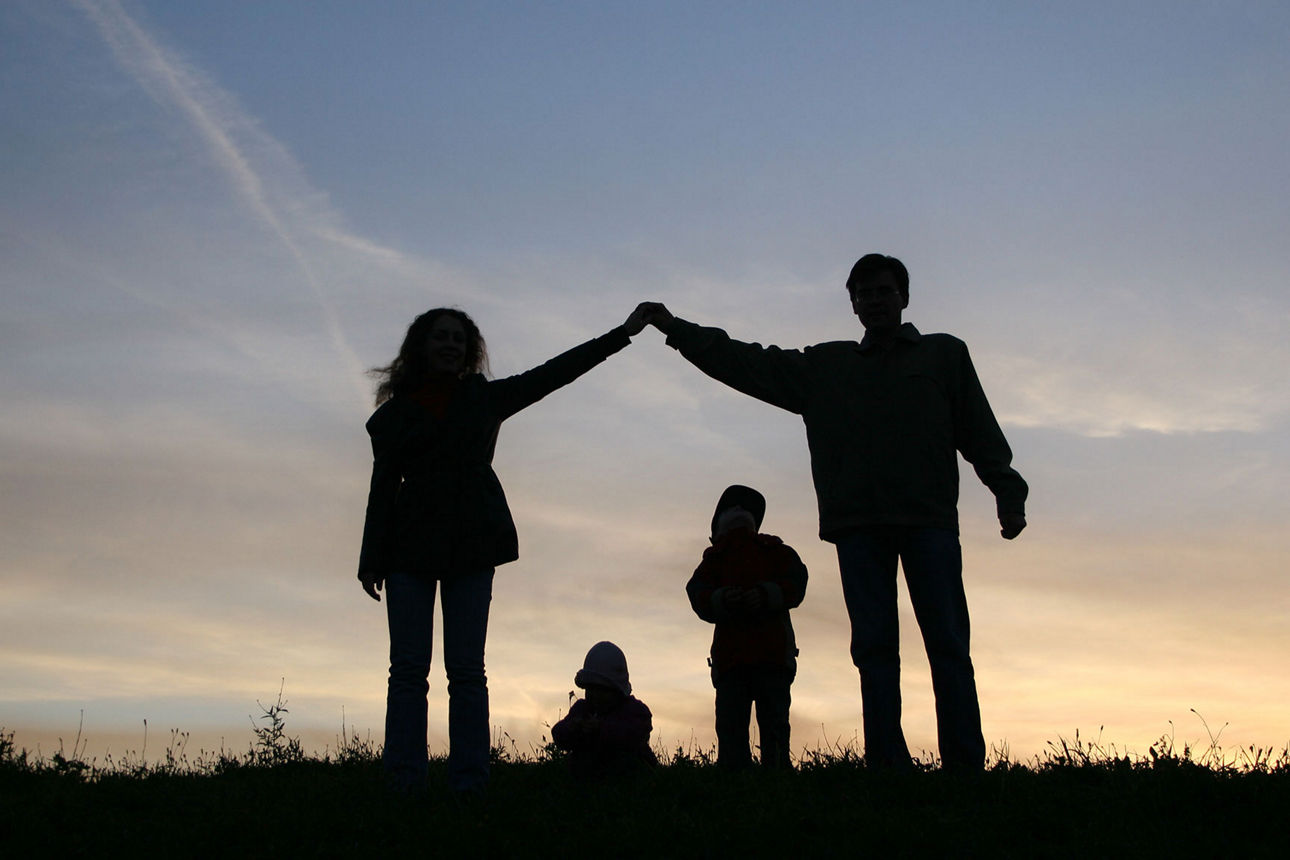Eine Familie die ein Haus abbilden auf einer Wiese beim Sonnenuntergang.