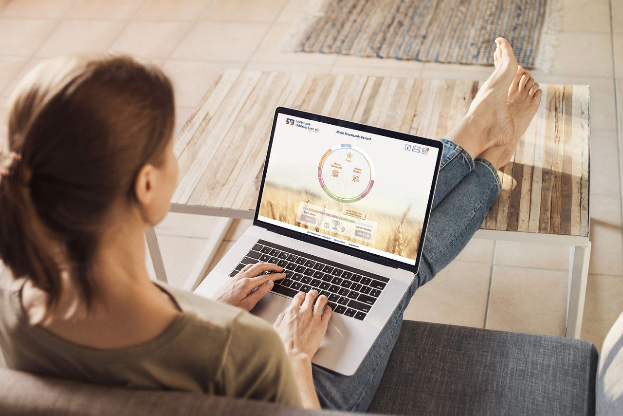 Eine Frau sitzt mit gekreuzten Beinen auf einer Couch und benutzt einen Laptop.
