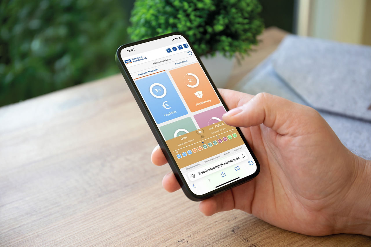 Smartphone wird in der Hand gehalten auf dem der Hausbank-Rechner zu sehen ist.