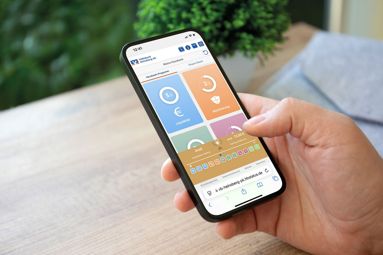 Smartphone wird in der Hand gehalten auf dem der Hausbank-Rechner zu sehen ist.