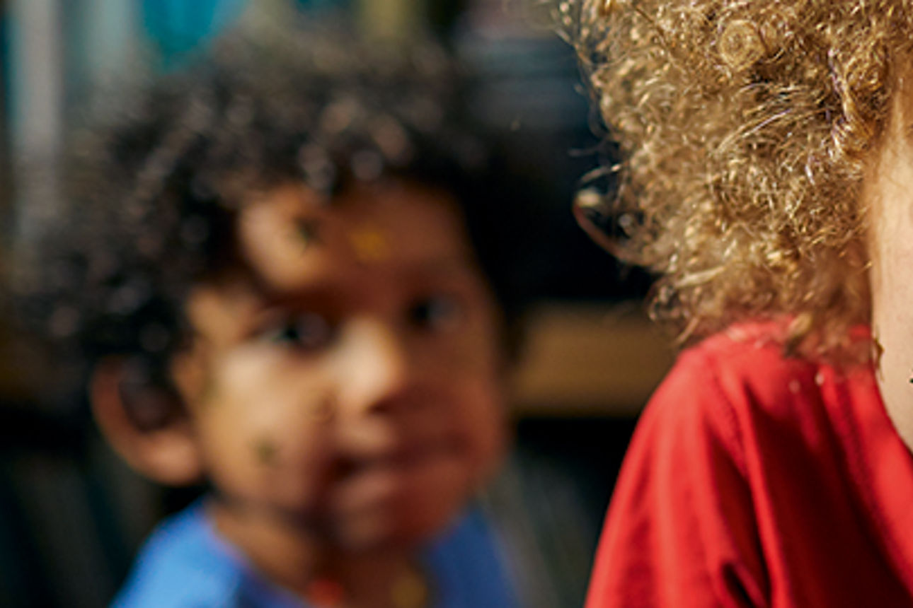 Lockenköpfiges Kind mit Sternenaufklebern im Gesicht, das lustige Gesichter in die Kamera macht