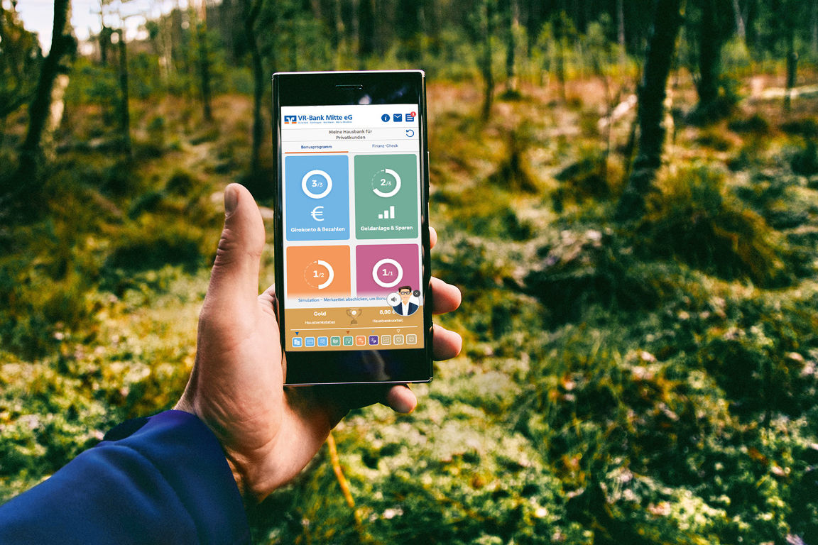 Ein Handy mit Hinweis zum Hausbankmodell wird von einer Hand im Wald gehalten