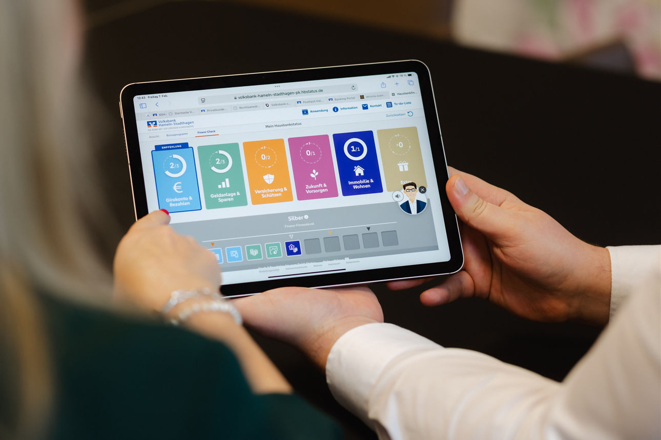 Zwei Personen, die gemeinsam auf ein Tablet schauen, auf dem die Übersicht des Hausbankprogramms dargestellt ist.