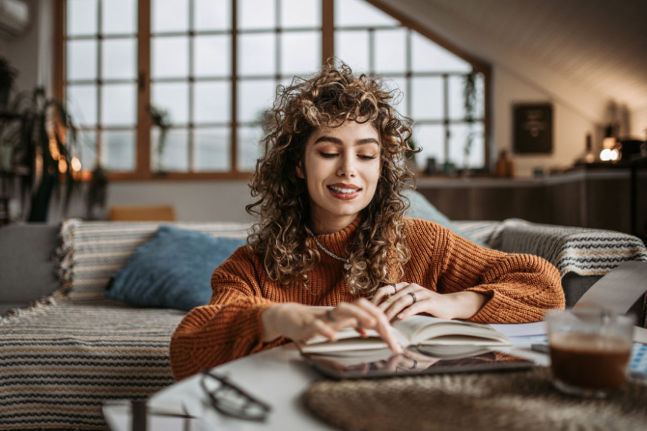 Eine Frau sitzt im Wohnzimmer und liest ein Buch.