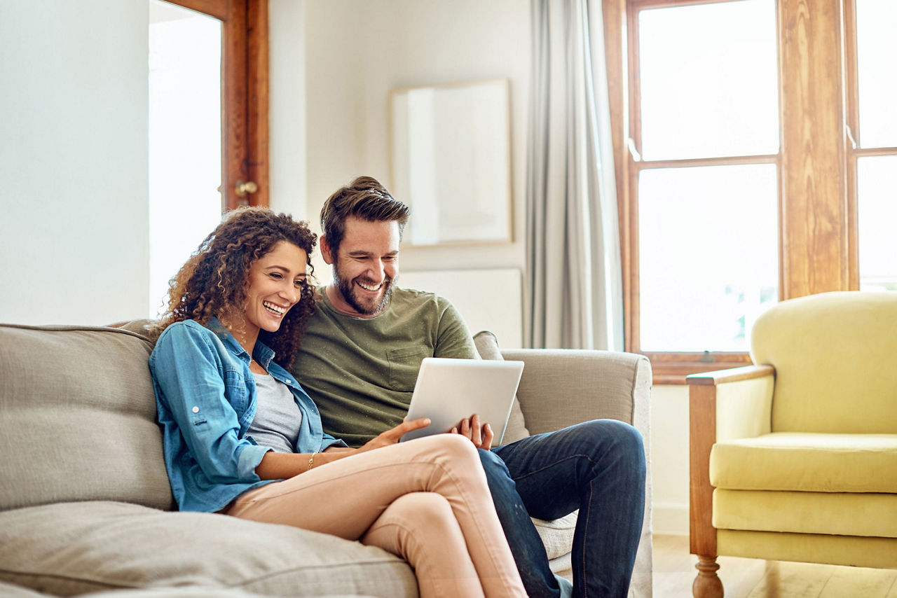Glückliches junges Paar sitzt auf dem Sofa und schaut auf den Bildschirm eines Laptops