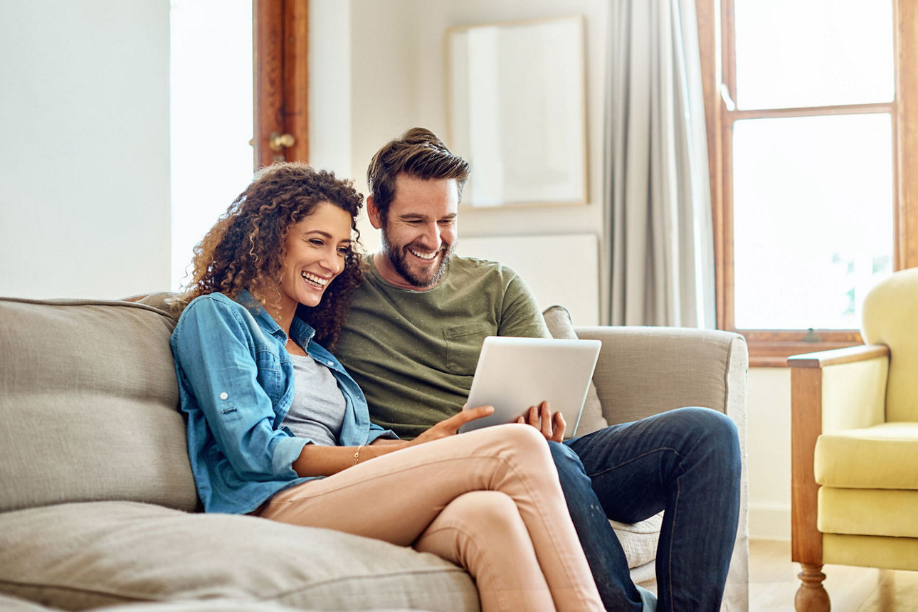 Glückliches junges Paar sitzt auf dem Sofa und schaut auf den Bildschirm eines Laptops