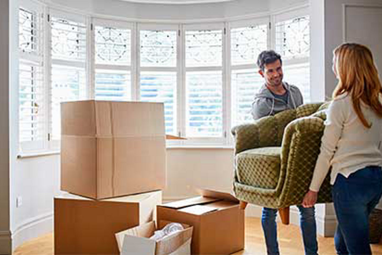Paar trägt einen Sessel in eine leere Wohnung