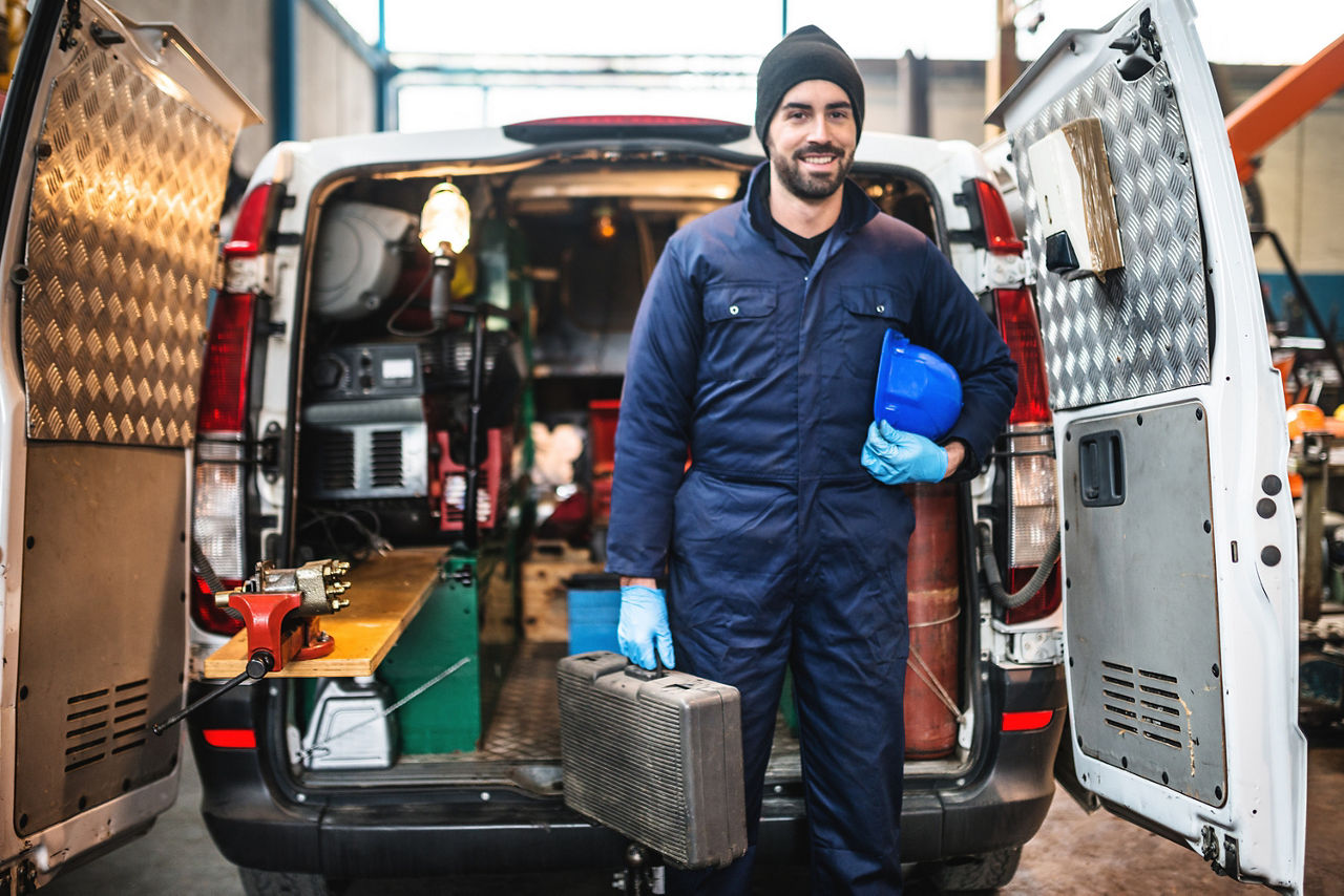Handwerker steht mit Werkzeugkoffer vor einem Transporter
