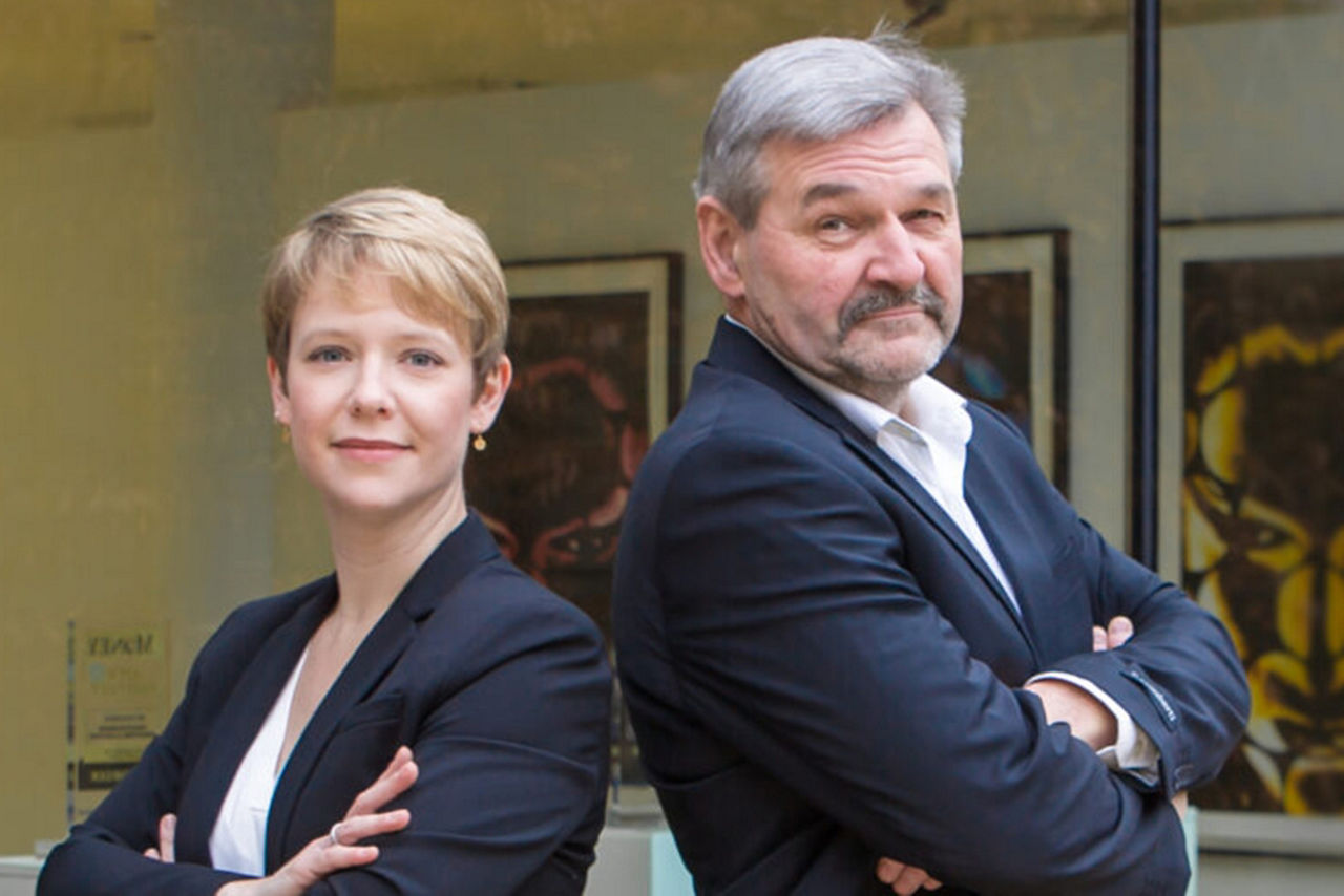 Frau und Mann stehen mit verschränkten Armen vor verschiedenen Bildern