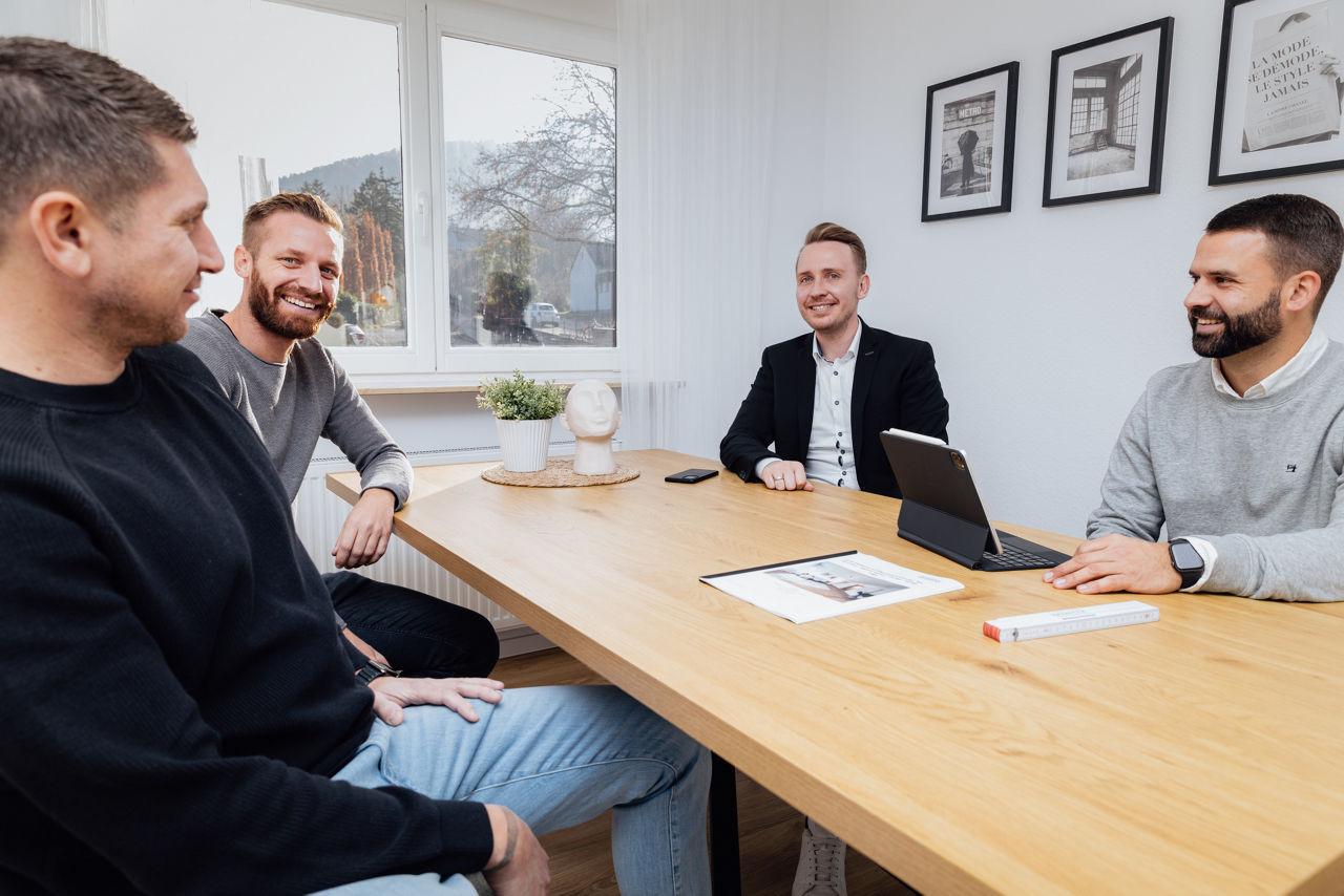 Mehrere Personen sitzen an einem Tisch innerhalb einer Immobilie der HAVANOLA Immobilien GmbH und besprechen Unterlagen zur Projektentwicklung und Vermarktung.