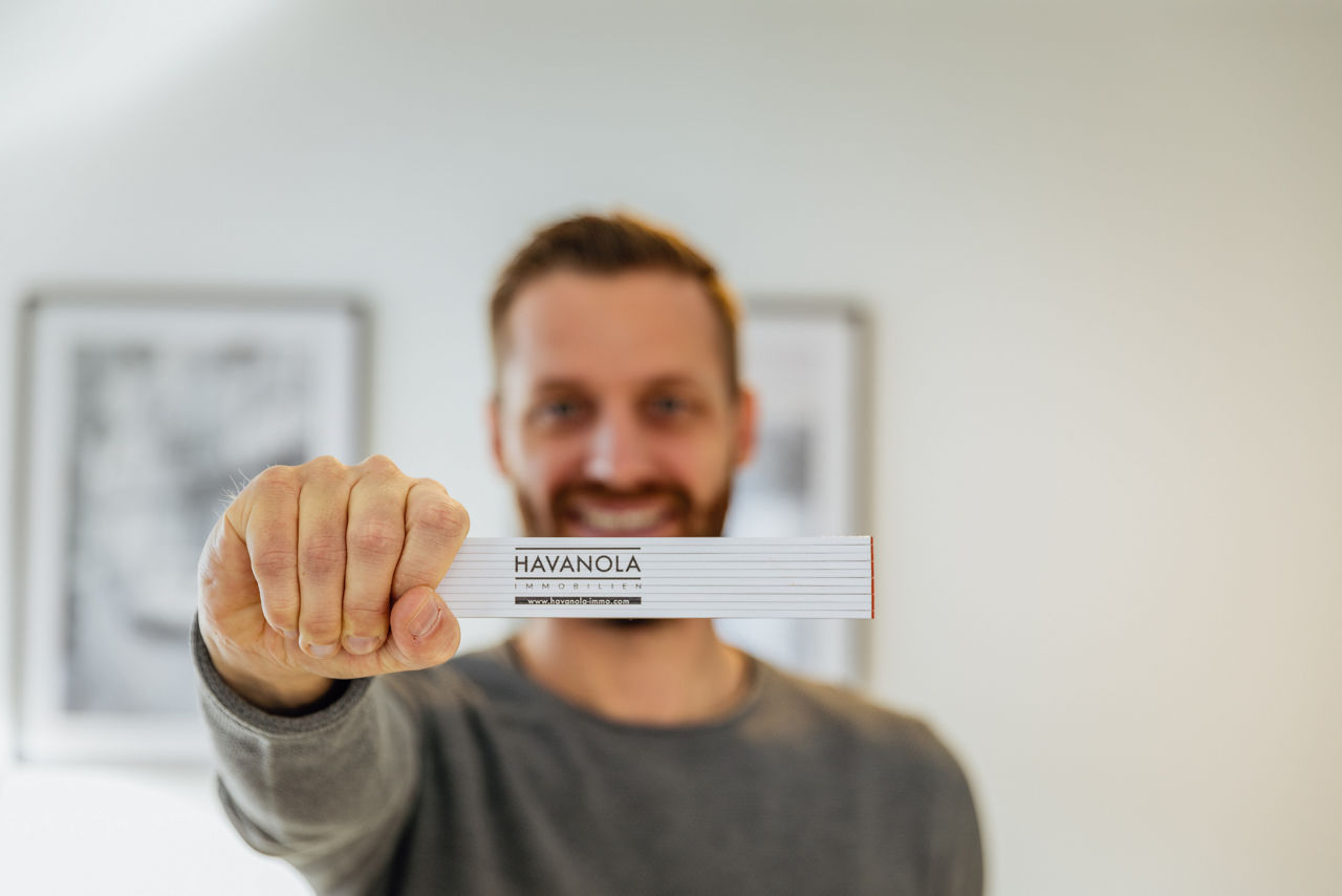 Detailaufnahme eines Maßstabs mit Logo der HAVANOLA Immobilien GmbH, gehalten im Vordergrund als Symbol für Planung, Maßarbeit und Projektentwicklung.