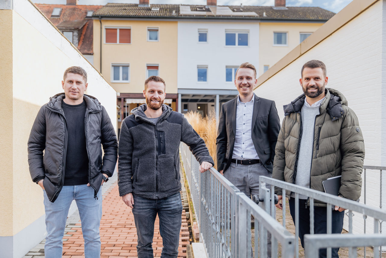 Mehrere Personen stehen im Außenbereich eines Wohnprojekts der HAVANOLA Immobilien GmbH, umgeben von sanierten Gebäuden und gestalteten Zugangswegen.