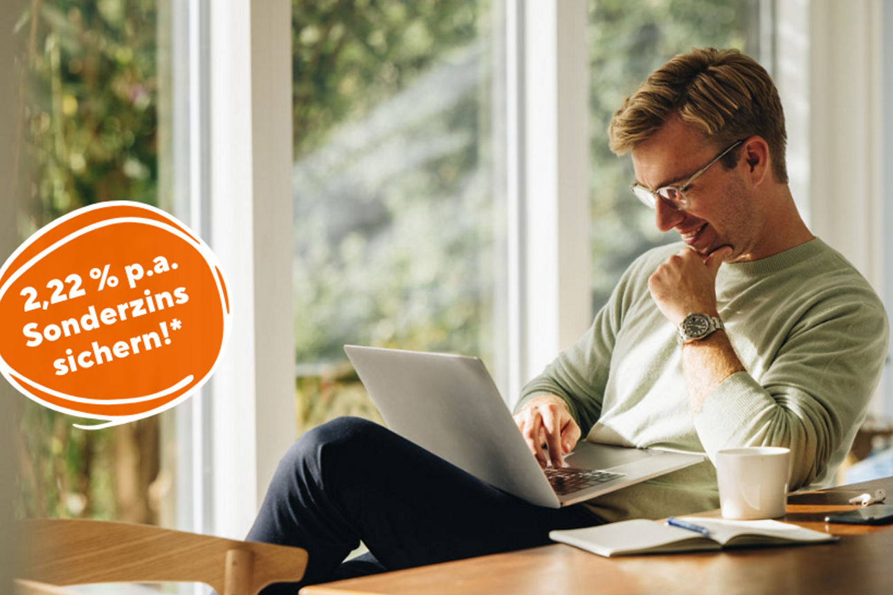 Mann sitzt lächelnd am Laptop, daneben ein Hinweis auf 2,22 % p.a. Sonderzins.