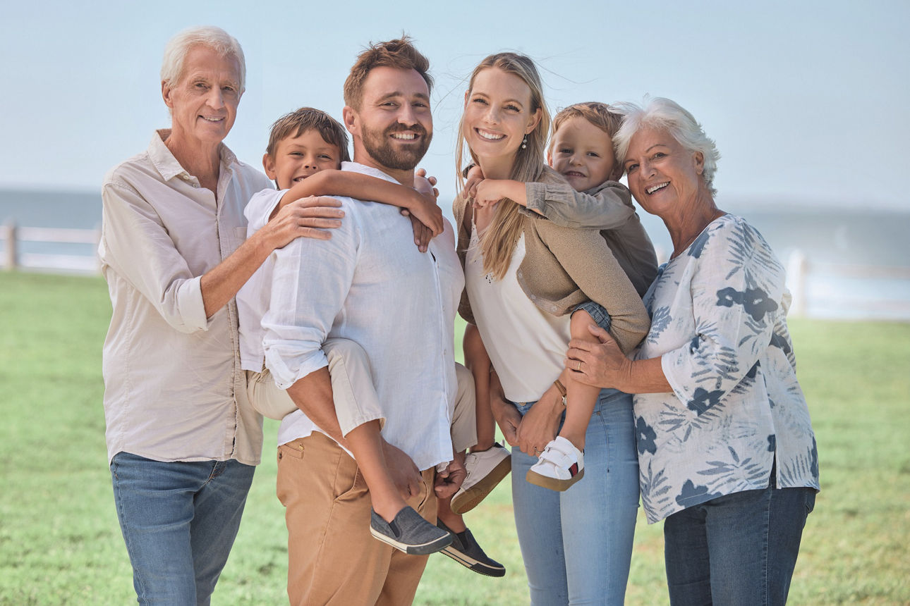 Eine 6-Köpfige Familie, darunter zwei Großeltern, steht auf einer Wiese und lächelt in die Kamera