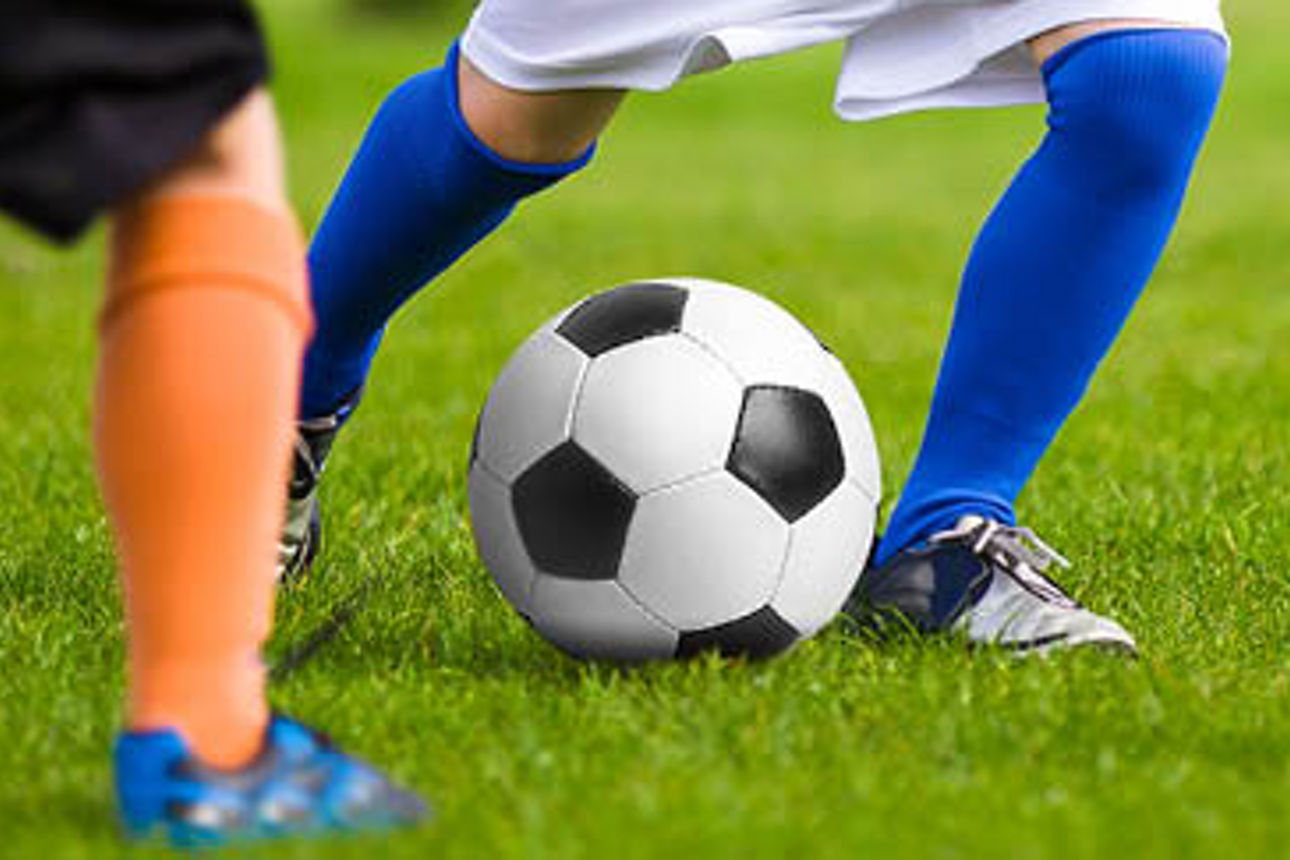 Zwei Kinder die auf einer grünen Wiese Fußball spielen