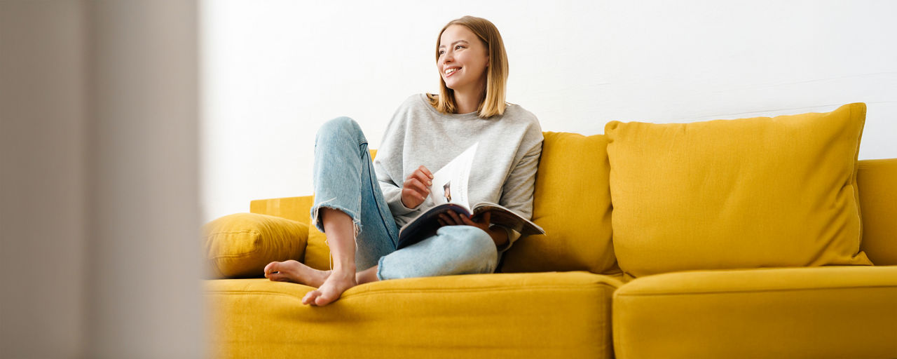 Frau sitzt mit Magazin auf gelbem Sofa