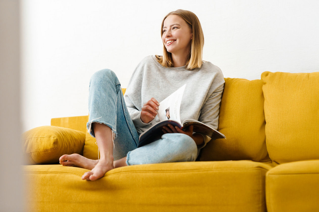 Frau sitzt mit Magazin auf gelbem Sofa