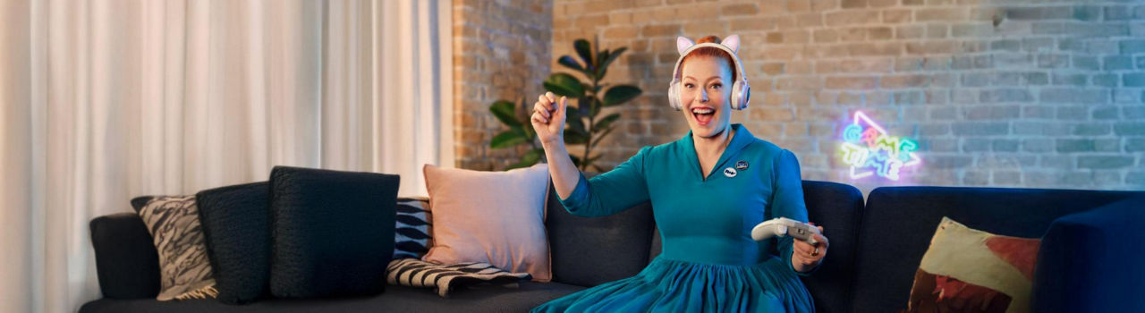 Eine Frau sitzt auf der Couch mit einem Controller in der Hand und freut sich
