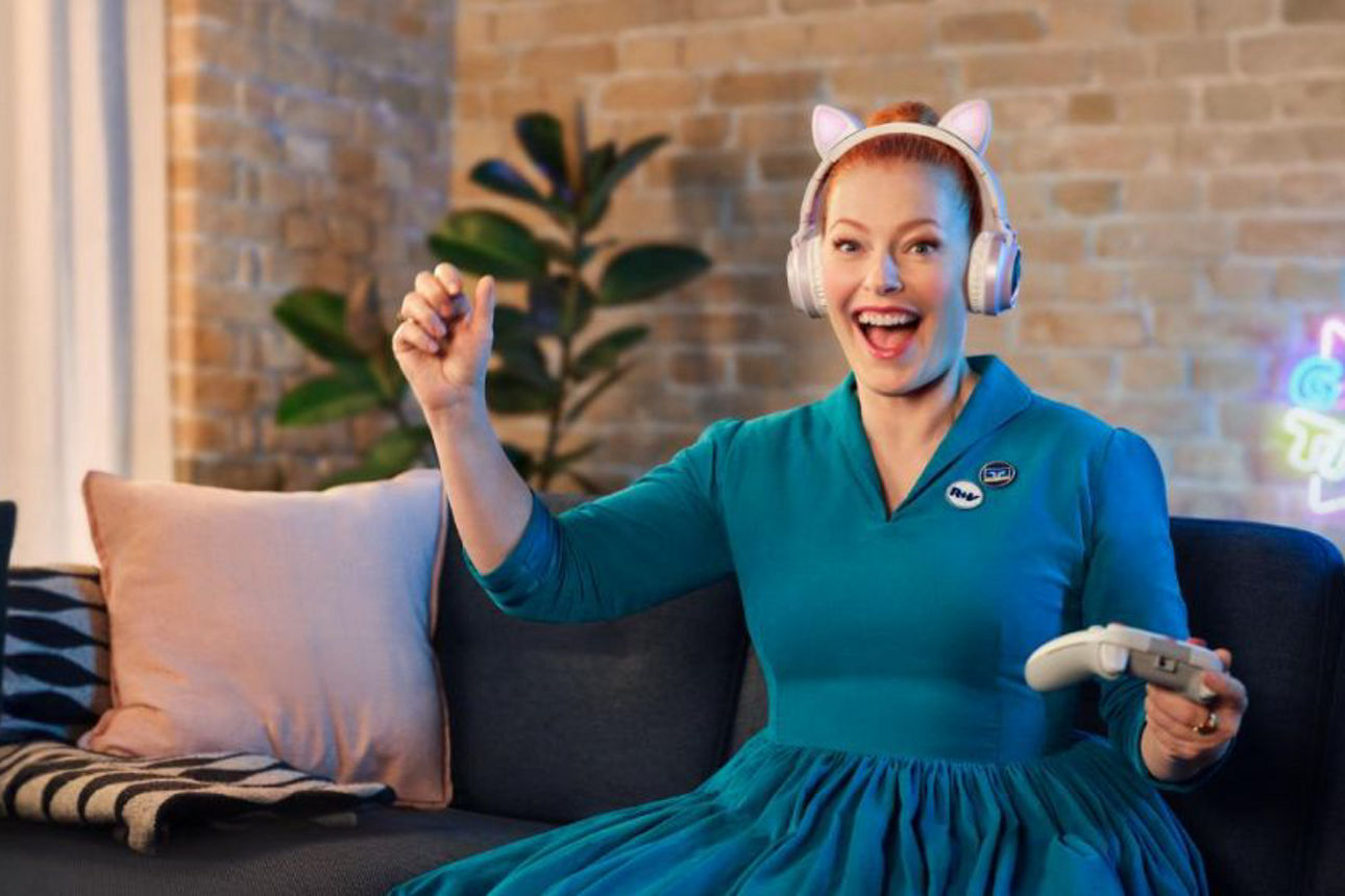 Eine Frau sitzt auf der Couch mit einem Controller in der Hand und freut sich