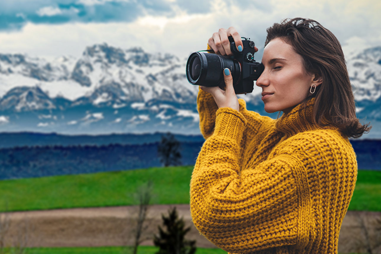 Frau mit Kamera steht vor Alpenpanorama