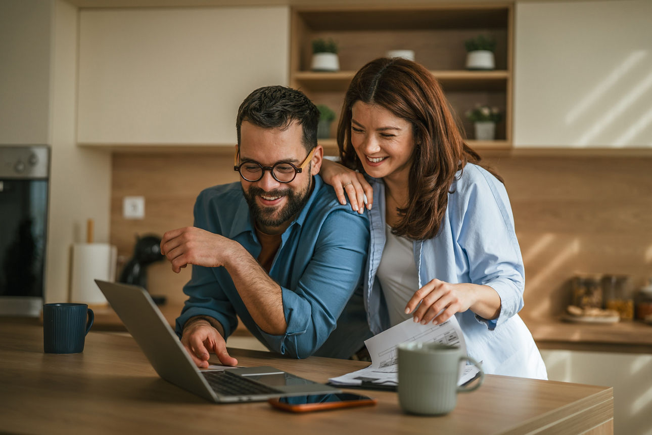Ein junges Paar steht in der Küche und schaut auf einen Laptop. 