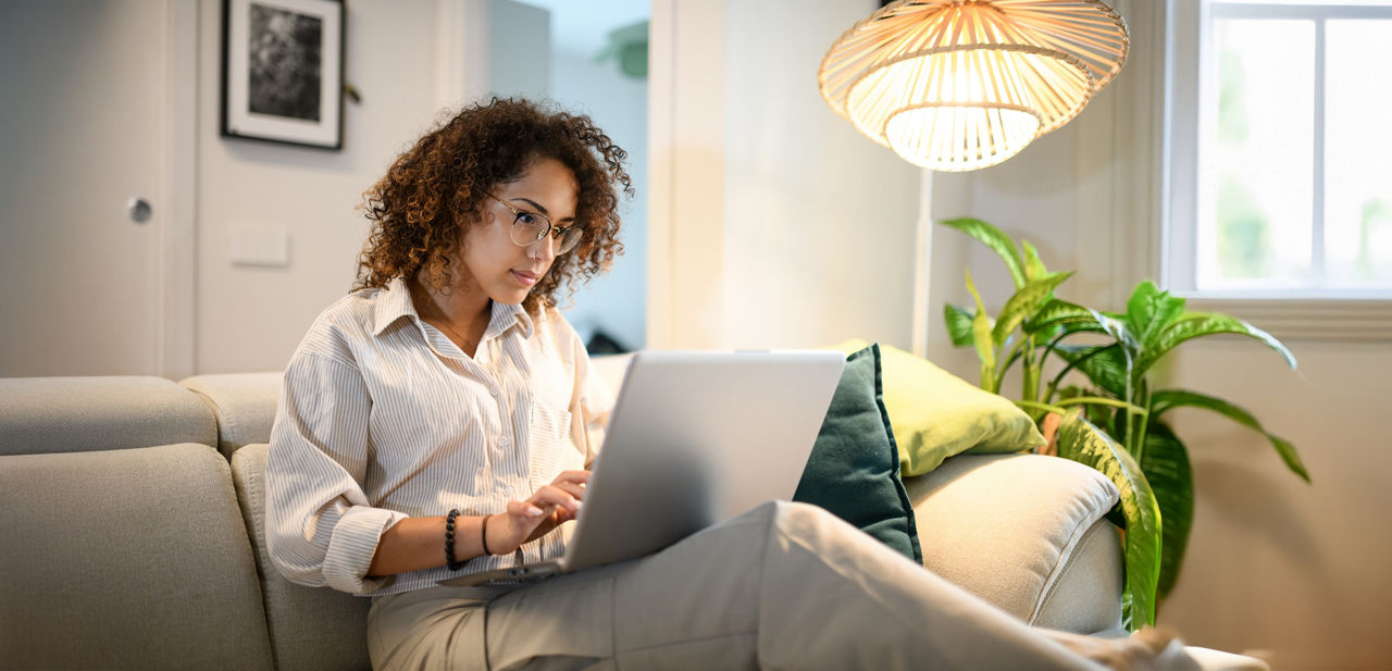 Frau sitzt mit Laptop auf dem Sofa