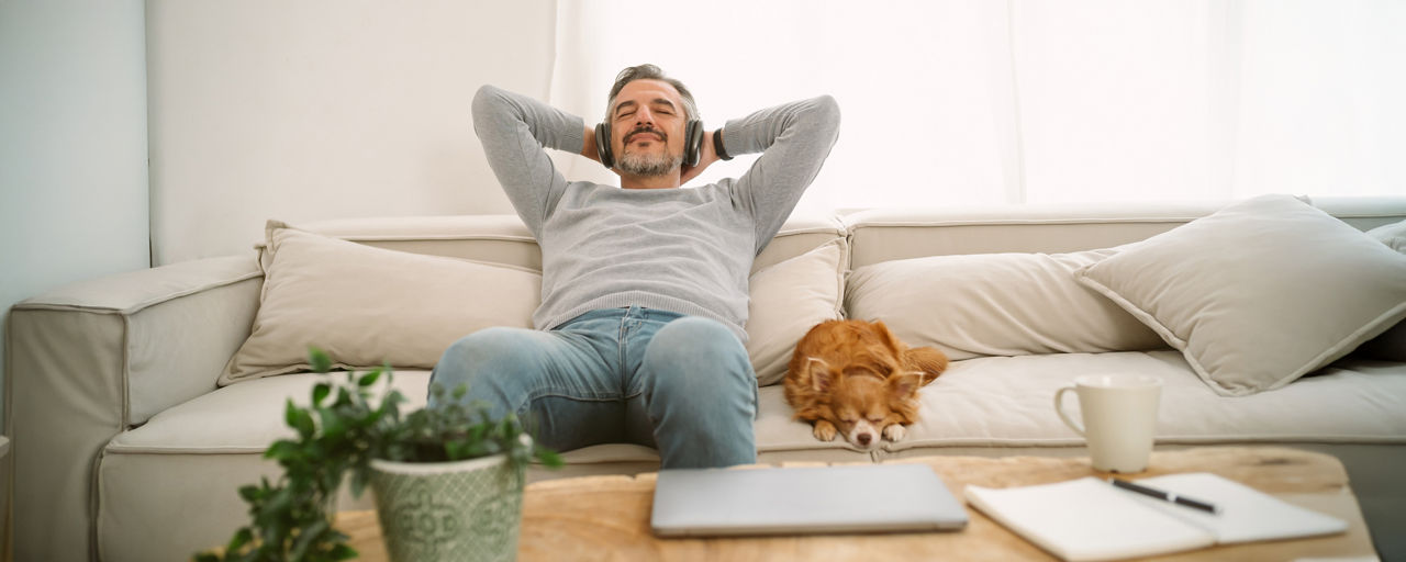 Mann entspannt auf der Couch. Neben ihm liegt sein Hund