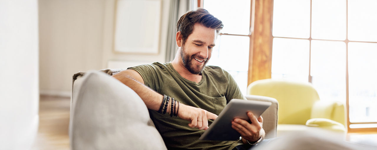 Mann sitzt mit Tablet auf der Couch und informiertsich über die Baufinanzierung