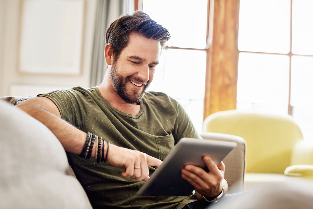 Mann sitzt mit Tablet auf der Couch und informiertsich über die Baufinanzierung
