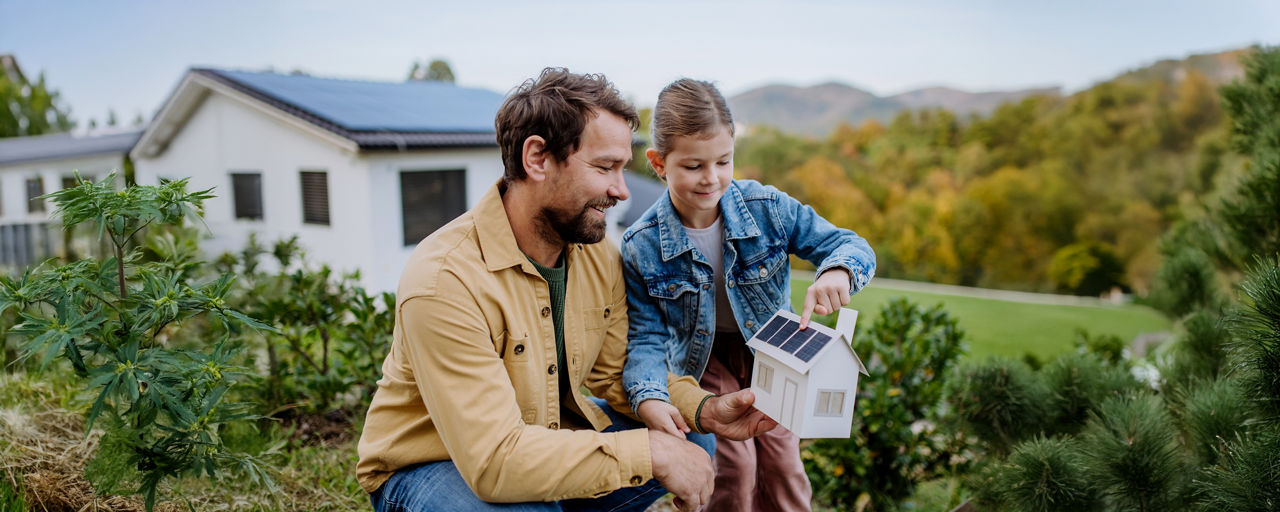 Vater mit Tochter schauen ein kleines Papphaus an.
